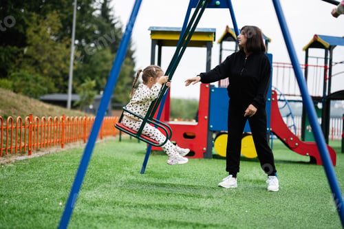 Preview: Mother and child playing on swing at colorful playground