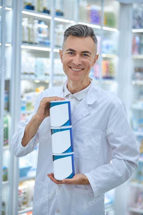 Preview: Smiling friendly pharmacist demonstrating new healthcare products at the drugstore