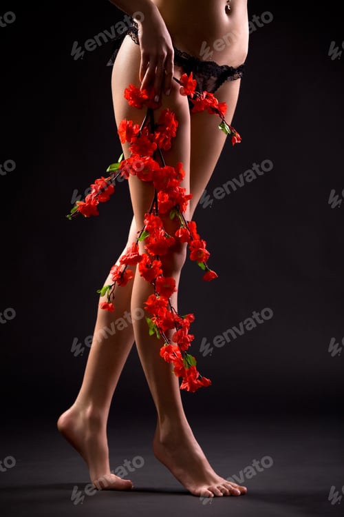 Preview: Legs of young woman wearing sexy black panties and holding red flowers in hand over dark background