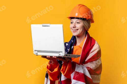Preview: worker in helmet and orange overalls holding laptop computer with USA flag