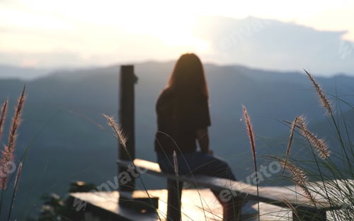 Preview: Rear view of a woman sitting and looking at a mountains view before sunset