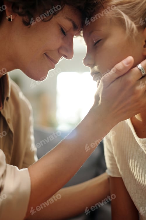 Preview: Happy young woman touching her cute daughter by hand and forehead