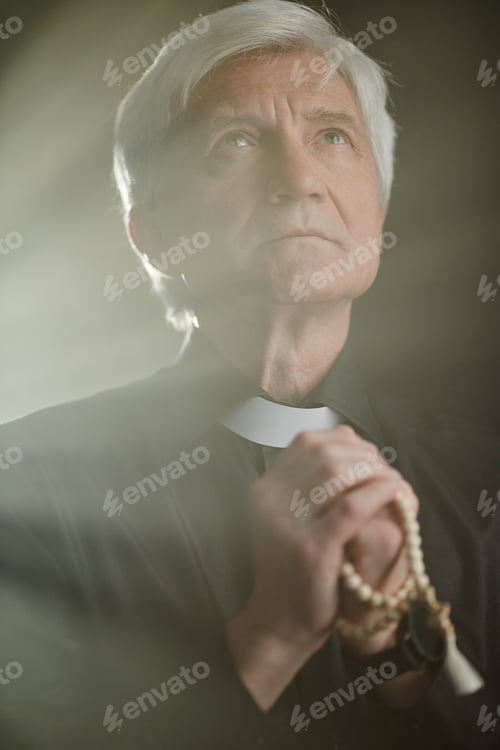 Preview: Vertical white haired senior priest praying with rosary in serene god rays