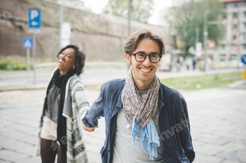 Preview: Multiethnic happy couple walking outdoors city hand in hand smiling
