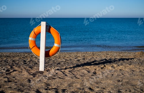 Preview: Bright orange lifebuoy on a sandy beach on a Sunny summer day.