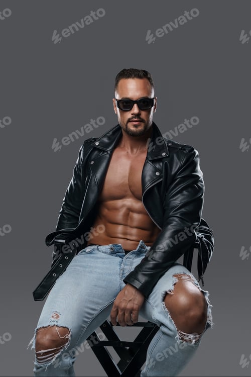 Preview: Handsome male model seated on a studio chair against grey backdrop