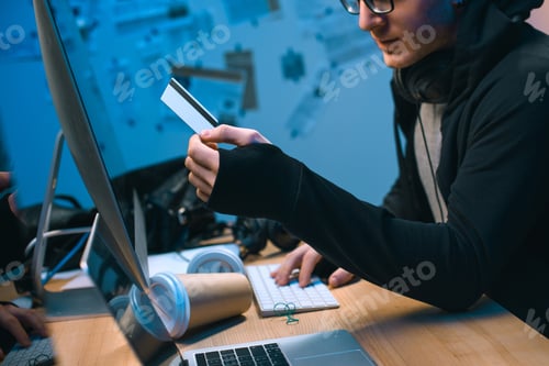 Preview: cropped shot of hacker holding stolen credit card in dark room