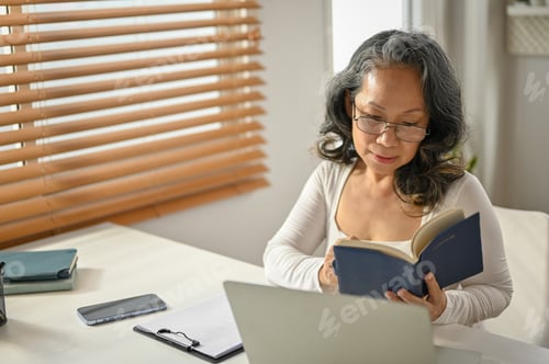 Preview: Relaxed 60s Asian-aged woman reading a book at her workspace. leisure and hobby concept
