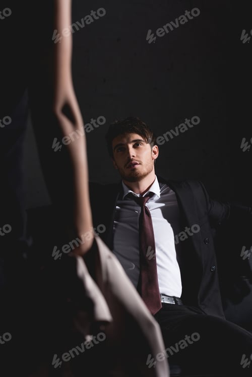 Preview: selective focus of man in suit sitting on couch opposite brunette woman on black background