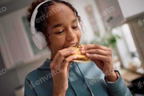 Preview: Black teenage girl eating sandwich in the kitchen.