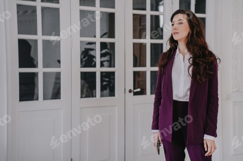 Preview: Attractive tired brunette businesswoman holds phone looking aside dressed in burgundy suit at office