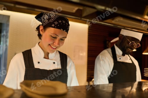 Preview: Happy young woman in uniform standing by counter and cooking food