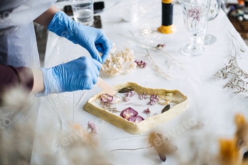 Preview: Hands arranging dried flowers into resin art piece, using sustainable materials for eco-friendly