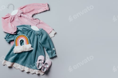 Preview: Blue, pink dress for baby girl with white hanger, rainbow toy, shoes on grey background