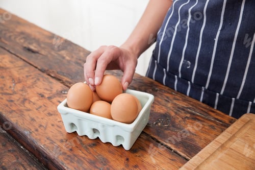 Preview: Woman's hand picking egg from carton on kitchen counter