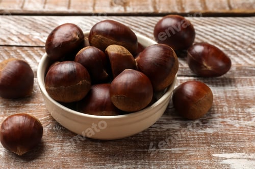 Preview: Sweet fresh edible chestnuts in bowl on wooden table, closeup