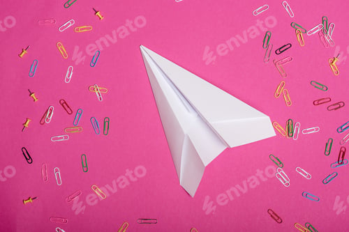 Preview: Top view of white paper plane and colorful paper clips isolated on pink