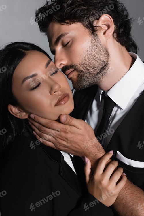 Preview: elegant man kissing sensual asian woman isolated on grey