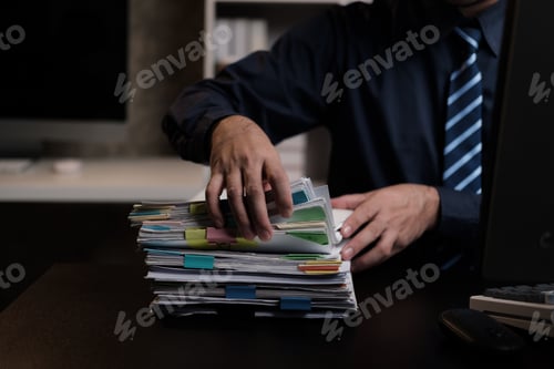 Preview: Close up view of businessman woking and gathering information from stack of document, working overti