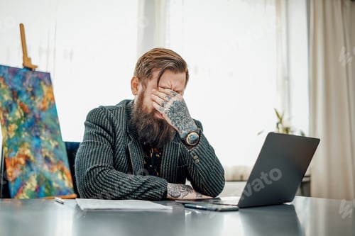 Preview: Bearded guy dressed in suit sits at table with a laptop and papers