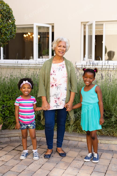 Preview: Portrait of african american grandmother holding hands of her granddaughters and smiling outdoors
