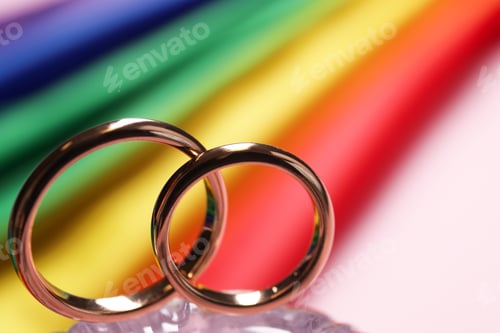 Preview: Wedding rings against rainbow LGBT flag, selective focus