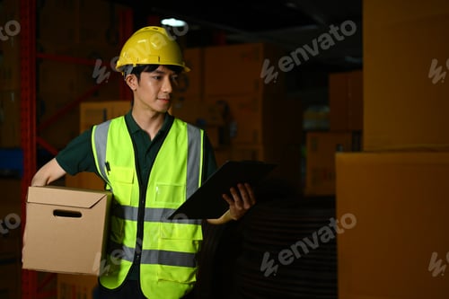 Preview: Warehouse worker carrying a cardboard box standing in retail warehouse.