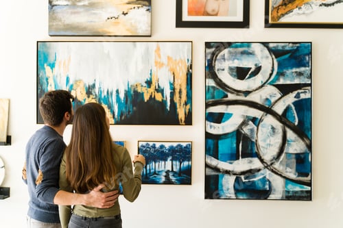 Preview: Rear view of a young woman and guy admiring the paintings of an art exhibition