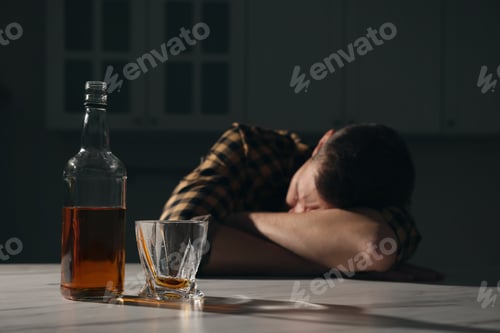 Preview: Addicted man sleeping at table in kitchen, focus on alcoholic drink. Space for text