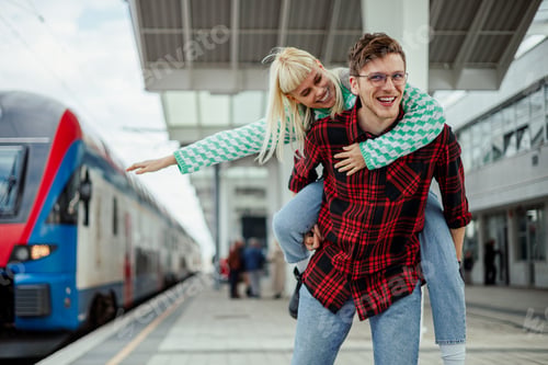 Preview: Woman with open arms is riding man's back on a railway station
