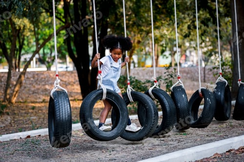 Preview: A curly girl black skin playing on passes an obstacle on tires in a rope Park.