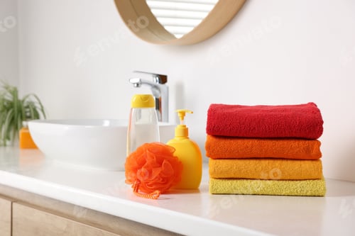 Preview: Stack of fresh terry towels, cosmetic products and sponge on counter near sink
