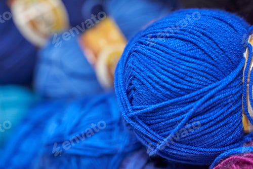 Preview: Close-up of vibrant blue yarn balls in knitting basket with colorful background for crafting