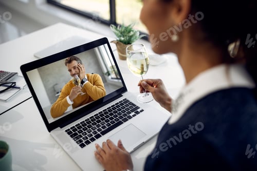 Preview: Close-up of couple drinking wine while having online date over a laptop.