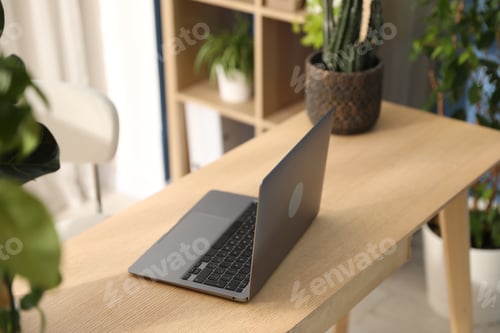 Preview: Stylish workplace with laptop on wooden desk and floral decor in office. Biophilic interior design