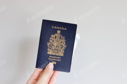 Preview: Woman’s hand holding a Canadian passport in front of white background