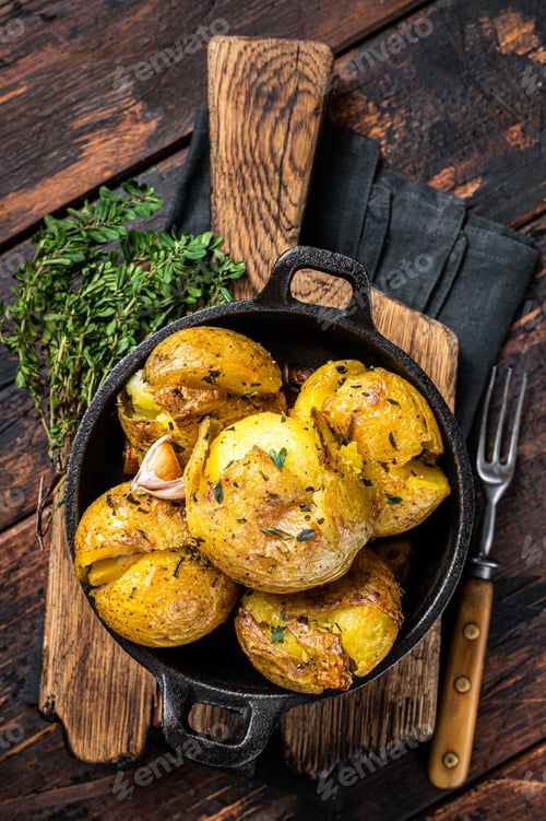 Preview: Crushed, Broken potatoes baked in oil with herbs. Wooden background. Top view
