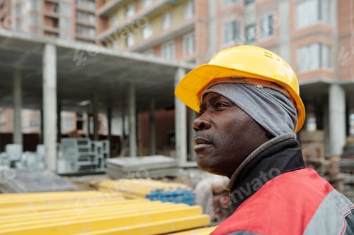 Preview: African American male builder in workwear and hardhat looking aside