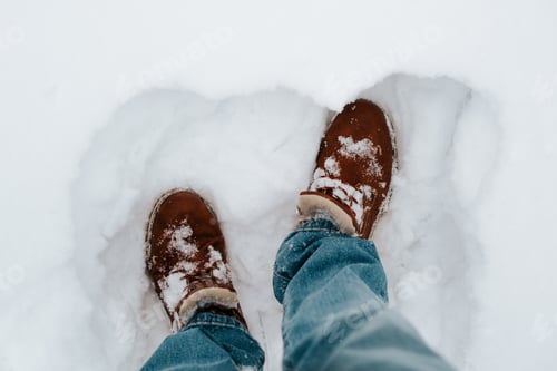 Preview: Close-up of man wearing blue jeans and winter brown boots standing in snowdrift outdoors, top view