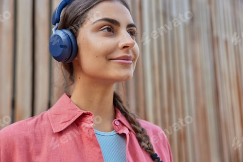 Preview: Close up shot of pleased millennial girl enjoys favorite music from playlist dreams about rest walks