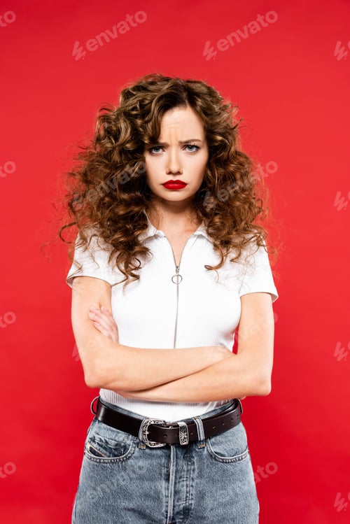 Preview: attractive offended curly girl with crossed arms, isolated on red