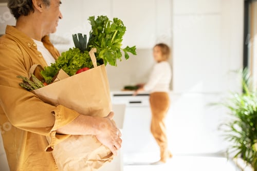Preview: Senior man holding paper bag full of vegetables, receiving delivery from supermarket, kitchen