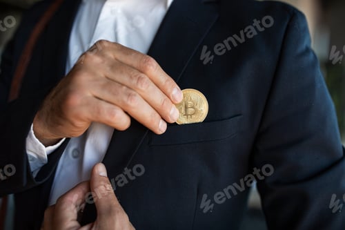 Preview: Male ceo manager in suit putting bitcoin coin in pocket, standing in office interior, closeup