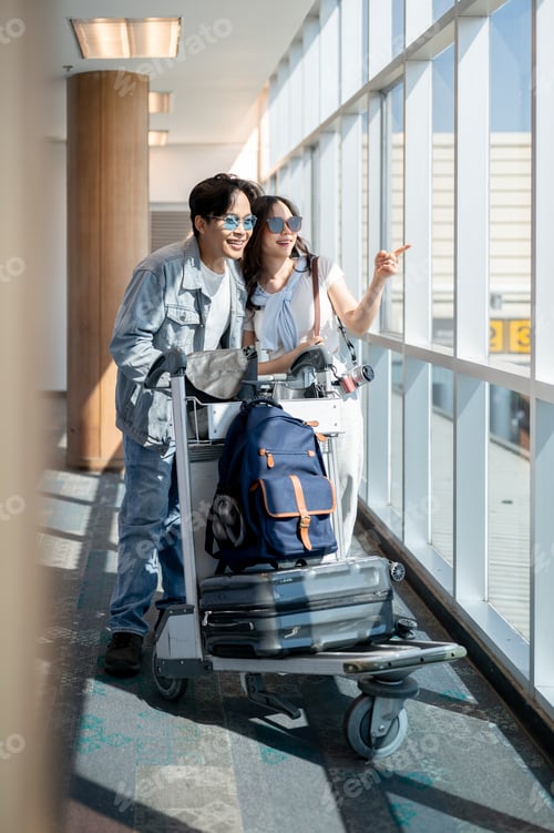 Preview: Asian tourist couple go on a trip man and woman walking with luggage cart looking around in airport.