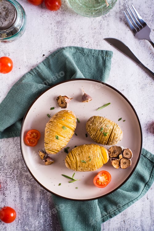 Preview: Baked hasselback potatoes with garlic and rosemary on a plate. Homemade lunch. Top and vertical view