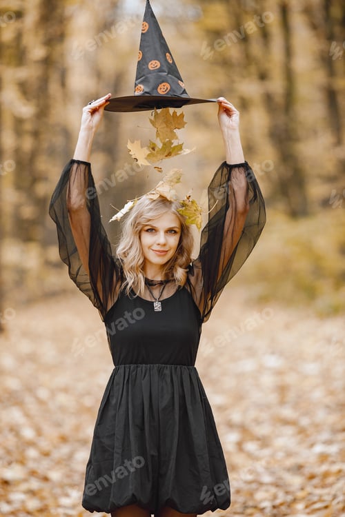 Preview: Young witch in forest on Halloween wearing black dress and cone hat
