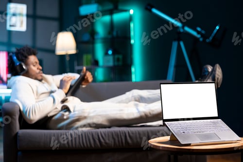 Preview: Man enjoying himself watching tv series in apartment, focus on mockup laptop.