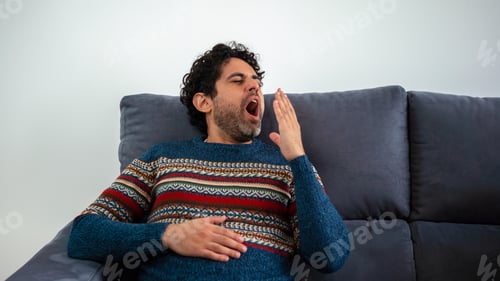 Preview: Man relaxing and yawing while sitting on couch home. bearded man sits on sofa