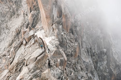 Preview: A mountaineer walks, seen from afar, along the spiers of a mountain.
