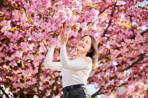 Preview: Woman allergic enjoying after treatment from seasonal allergy in front of blossom tree at spring.